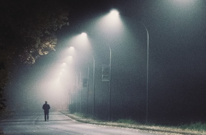 A silhouette of a person walking down a dark street lit only by street lights